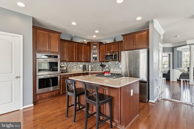 kitchen featuring appliances with stainless steel finishes, light stone counters, a center island, decorative backsplash, and glass insert cabinets