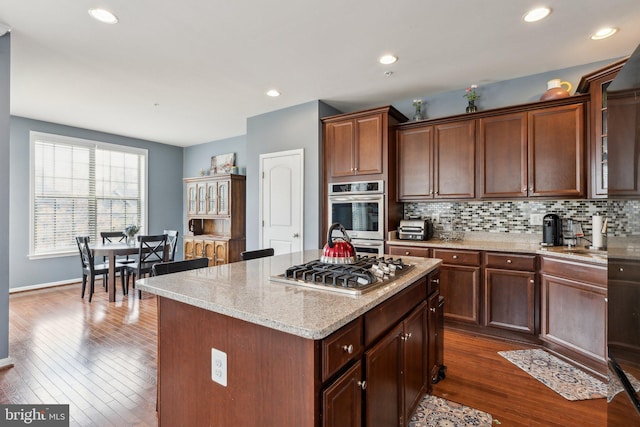 kitchen featuring decorative backsplash, a center island, light stone counters, dark wood finished floors, and appliances with stainless steel finishes