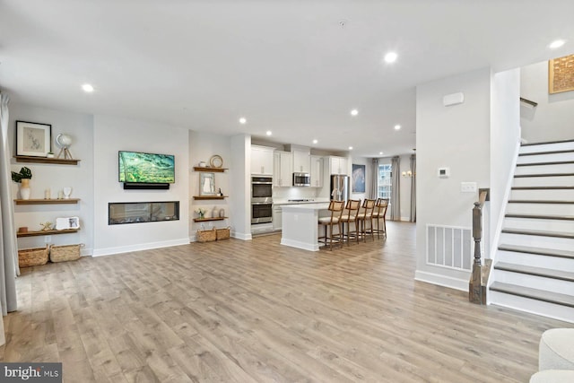 unfurnished living room featuring visible vents, light wood finished floors, baseboards, stairway, and recessed lighting