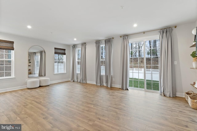 unfurnished living room with baseboards, light wood-type flooring, arched walkways, and recessed lighting