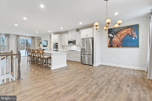 kitchen with light wood-style flooring, an island with sink, a notable chandelier, and appliances with stainless steel finishes