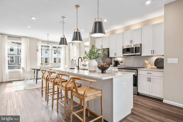 kitchen with light countertops, backsplash, a center island with sink, dark wood-style floors, and stainless steel appliances
