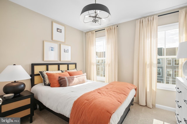 carpeted bedroom featuring baseboards, multiple windows, and a chandelier