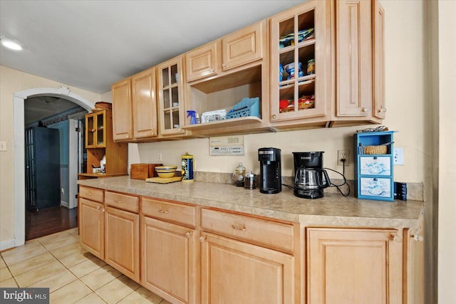 kitchen featuring light brown cabinets, light countertops, arched walkways, light tile patterned floors, and glass insert cabinets