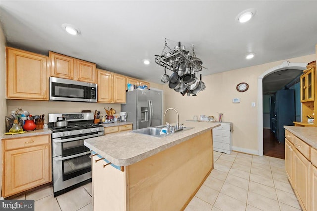 kitchen featuring light brown cabinetry, stainless steel appliances, arched walkways, and a sink