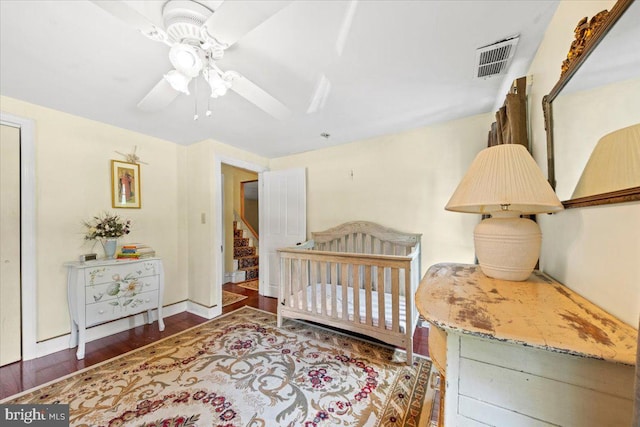 bedroom featuring visible vents, ceiling fan, wood finished floors, and a nursery area