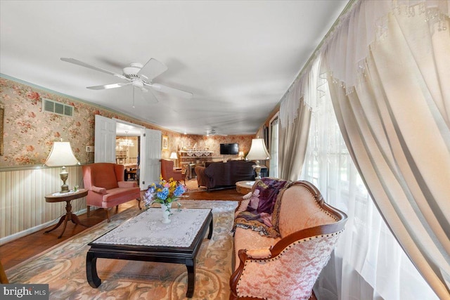 interior space with ceiling fan, visible vents, wainscoting, wood finished floors, and wallpapered walls