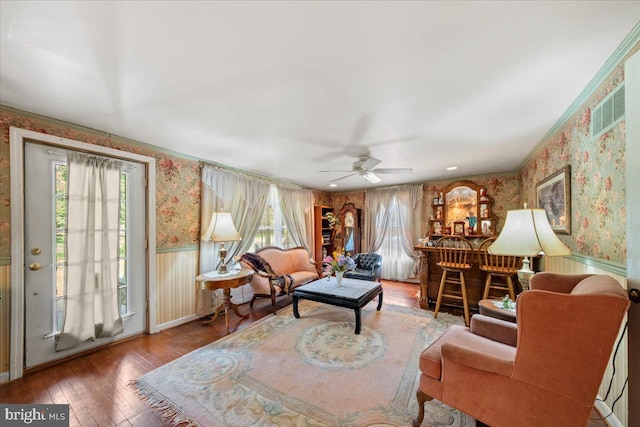 living area with a ceiling fan, a wainscoted wall, hardwood / wood-style floors, and wallpapered walls