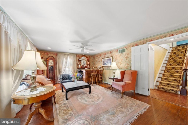 living area with visible vents, ceiling fan, stairway, wallpapered walls, and hardwood / wood-style flooring