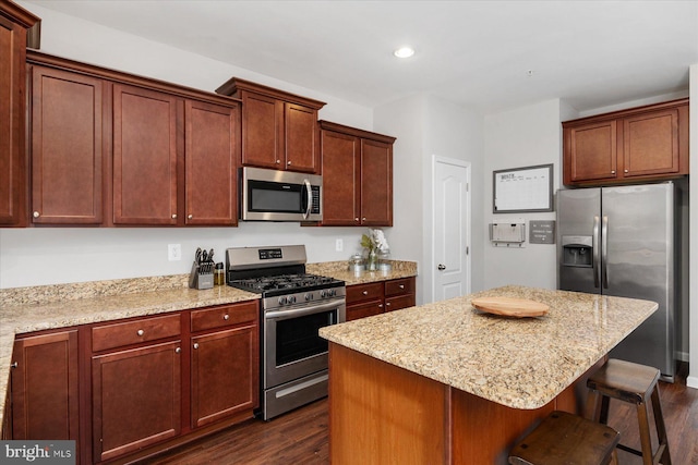 kitchen with light stone counters, dark wood-style flooring, appliances with stainless steel finishes, a kitchen island, and a breakfast bar area