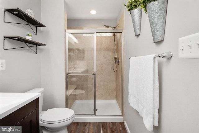 bathroom with toilet, vanity, a stall shower, and wood finished floors