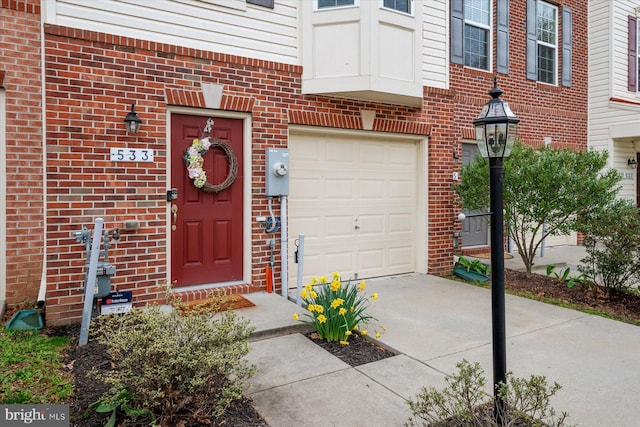 entrance to property featuring concrete driveway, brick siding, and an attached garage