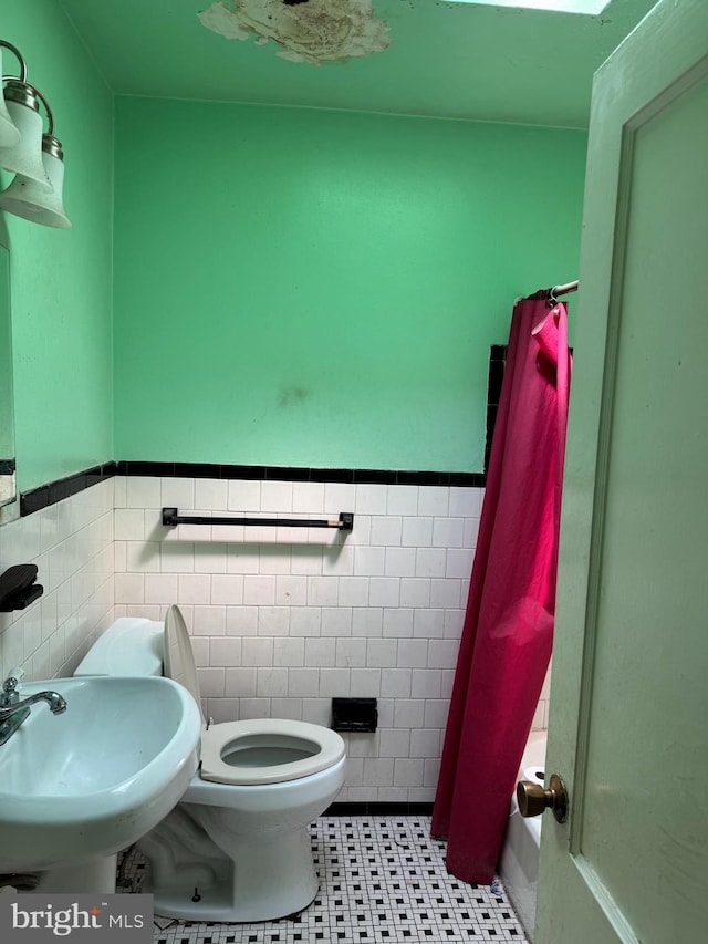 bathroom with tile walls, toilet, a sink, curtained shower, and wainscoting