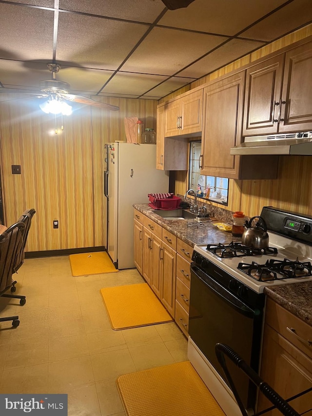 kitchen featuring under cabinet range hood, range with gas cooktop, a sink, ceiling fan, and freestanding refrigerator