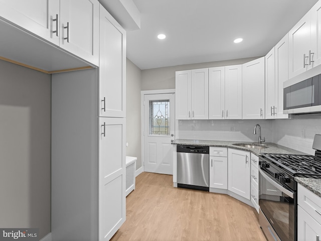 kitchen featuring white cabinets, stainless steel appliances, a sink, light wood-type flooring, and light stone countertops