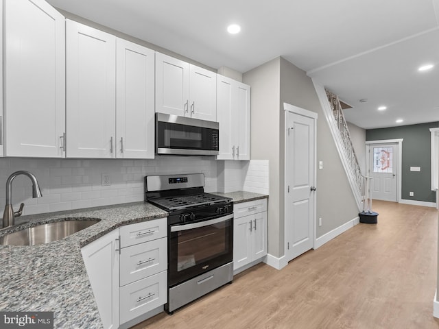 kitchen with tasteful backsplash, a sink, light wood-style flooring, baseboards, and appliances with stainless steel finishes