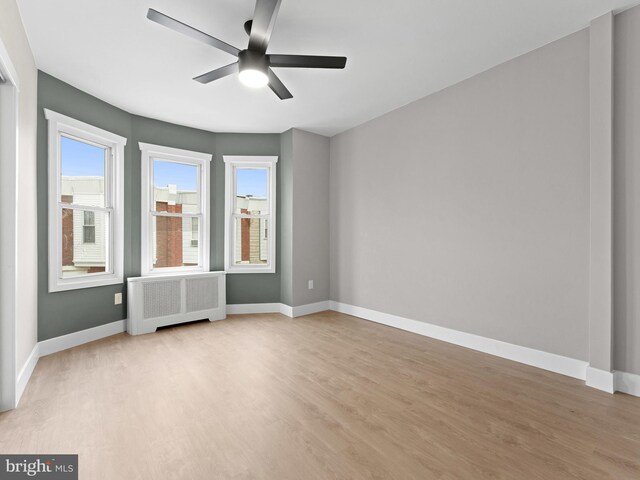 empty room featuring radiator heating unit, light wood-style flooring, baseboards, and ceiling fan