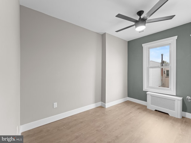 spare room featuring ceiling fan, baseboards, radiator heating unit, and light wood-style floors