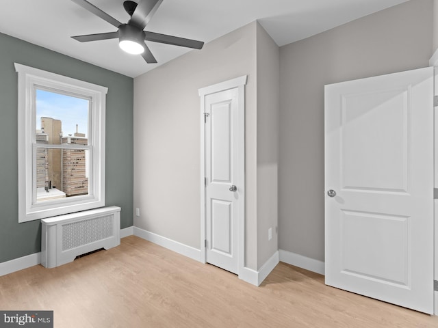 unfurnished bedroom featuring baseboards, radiator heating unit, and light wood-style flooring