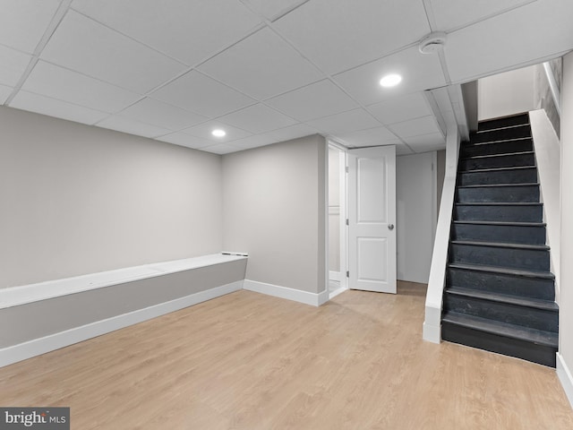 finished basement with a paneled ceiling, baseboards, recessed lighting, light wood-style floors, and stairs