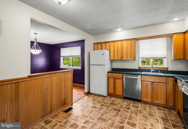 kitchen featuring appliances with stainless steel finishes, a textured ceiling, a sink, plenty of natural light, and dark countertops