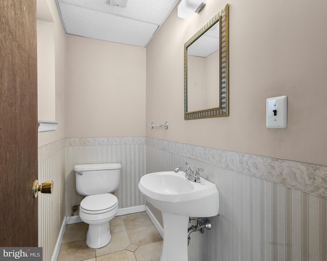 half bathroom with wainscoting, toilet, tile patterned floors, and a sink
