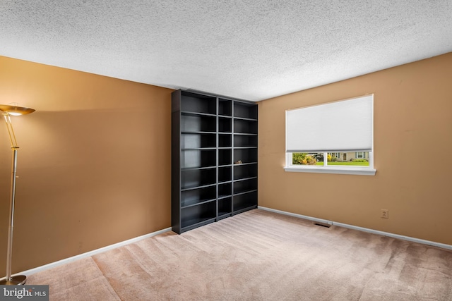 carpeted spare room featuring a textured ceiling and baseboards