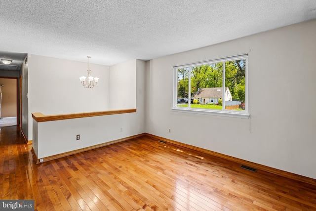 unfurnished room featuring hardwood / wood-style flooring, a textured ceiling, a chandelier, and baseboards