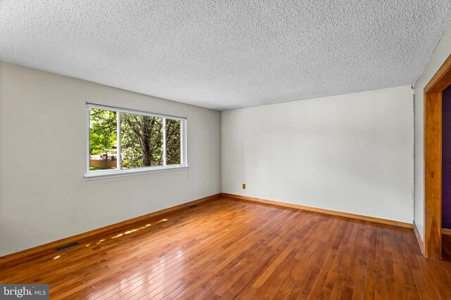 spare room with a textured ceiling, hardwood / wood-style flooring, and baseboards