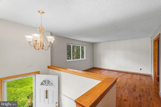 corridor with a textured ceiling, hardwood / wood-style flooring, a chandelier, and baseboards