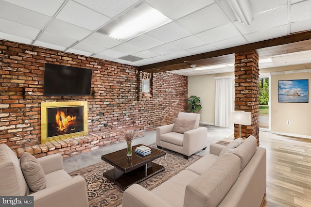 living area with a paneled ceiling, a brick fireplace, brick wall, wood finished floors, and baseboards