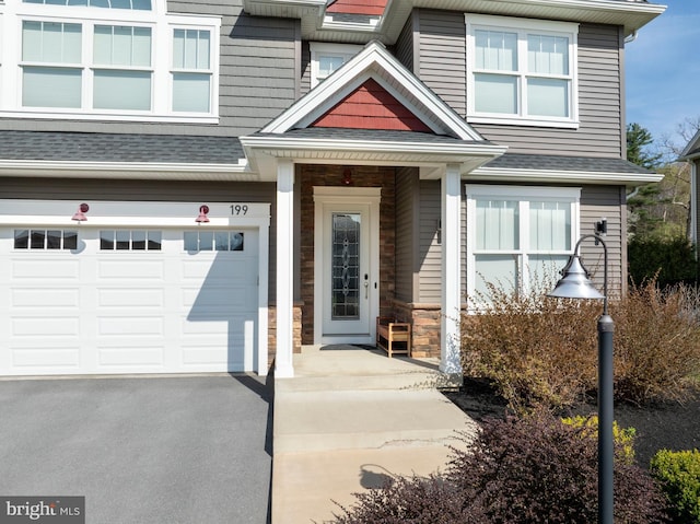 view of exterior entry with stone siding, driveway, roof with shingles, and a garage