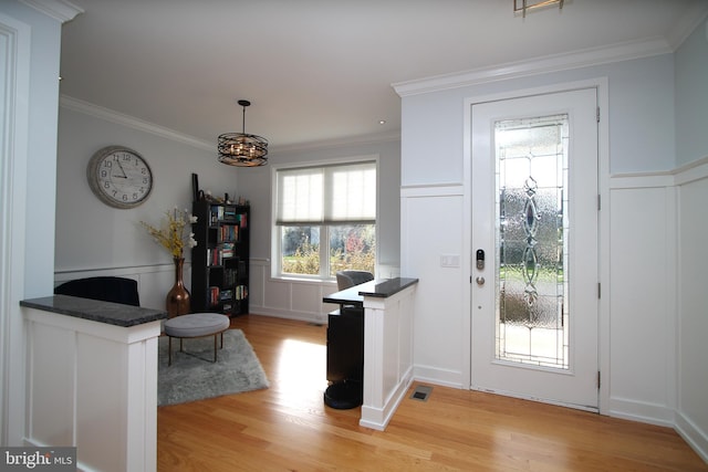 doorway to outside featuring a decorative wall, a wainscoted wall, light wood-type flooring, visible vents, and ornamental molding