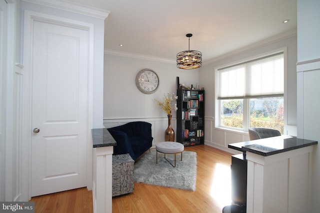 living area with an inviting chandelier, ornamental molding, a decorative wall, light wood-style floors, and a wainscoted wall