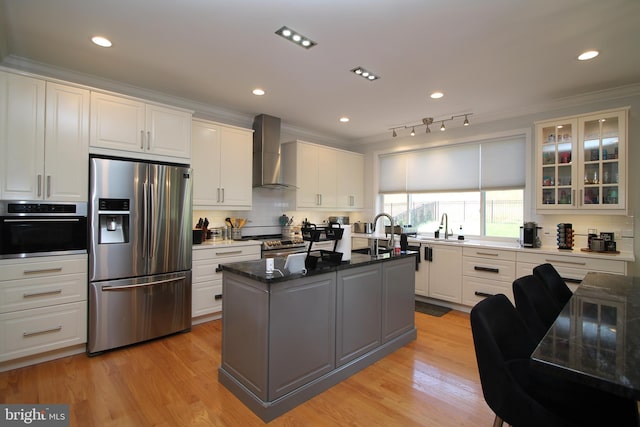 kitchen with wall chimney range hood, stainless steel appliances, crown molding, and white cabinets