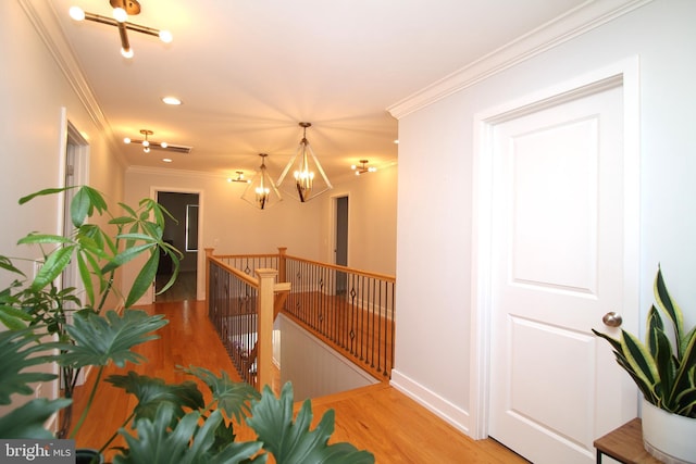 hallway with crown molding, an inviting chandelier, baseboards, an upstairs landing, and wood finished floors