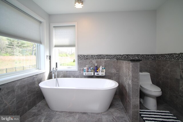 bathroom with wainscoting, a freestanding bath, toilet, and tile walls