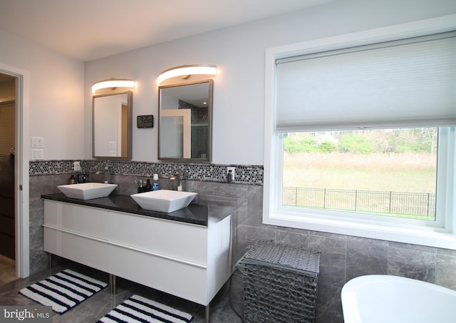 full bathroom with double vanity, a sink, a freestanding tub, and tile walls