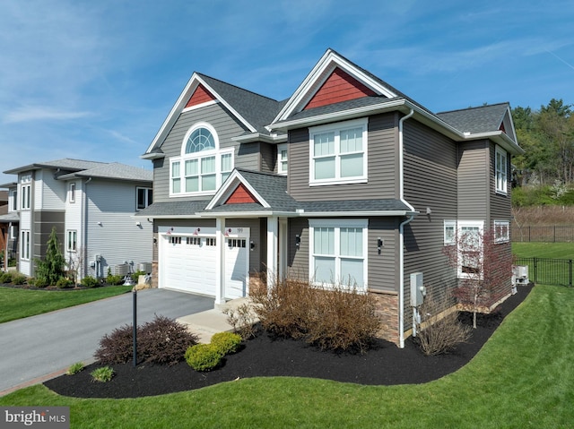craftsman-style house featuring driveway, roof with shingles, fence, a front lawn, and an attached garage