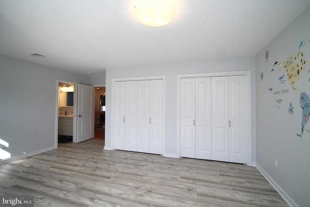 unfurnished bedroom featuring baseboards, multiple closets, visible vents, and wood finished floors
