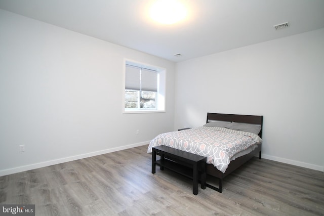 bedroom with baseboards, visible vents, and wood finished floors
