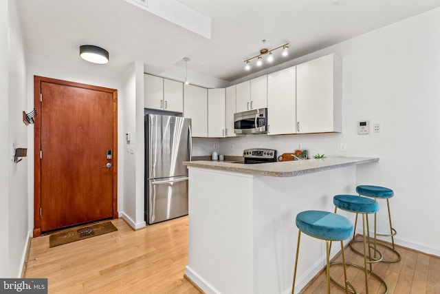 2412 17th St NW Unit 102, Washington, DC 20009 - kitchen with stainless steel appliances, light wood finished floors, a peninsula, baseboards, and a kitchen breakfast bar