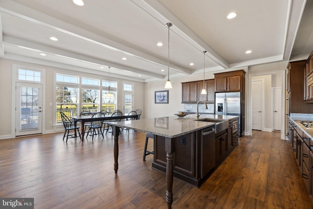 kitchen with dark wood-style flooring, stainless steel appliances, a center island with sink, a sink, and beam ceiling
