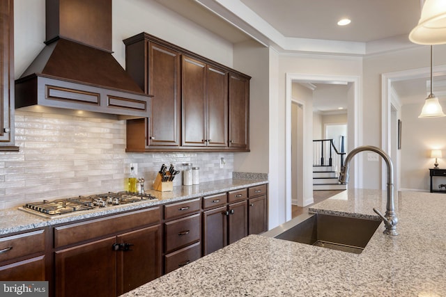 kitchen with stainless steel gas cooktop, backsplash, a sink, light stone countertops, and premium range hood