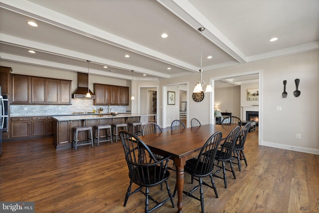 dining area with baseboards, a warm lit fireplace, beam ceiling, and dark wood-type flooring