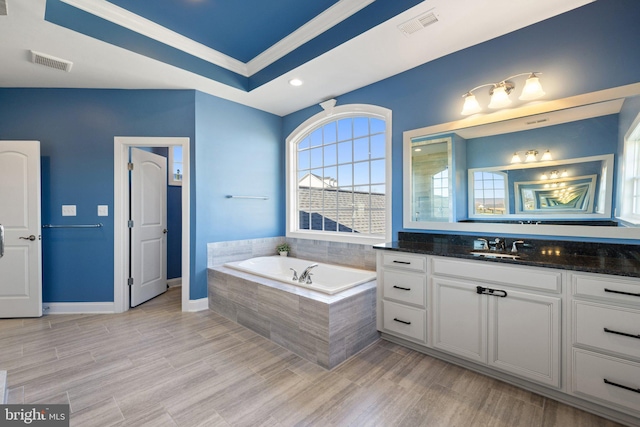 full bathroom with visible vents, vanity, a bath, and a raised ceiling