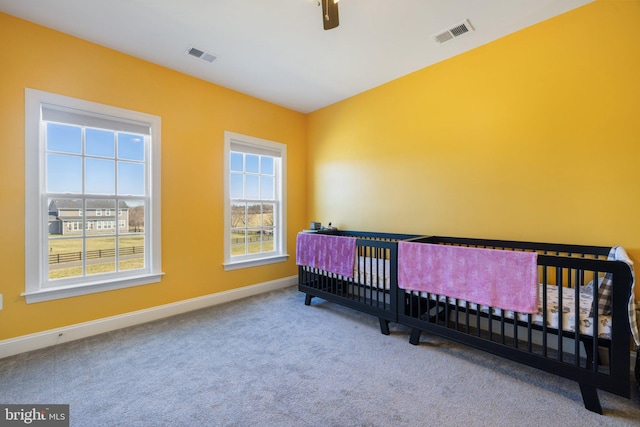 carpeted bedroom featuring baseboards, visible vents, ceiling fan, and a nursery area