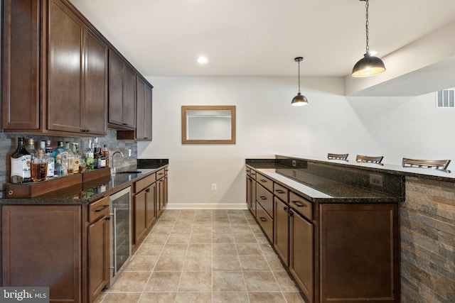 kitchen featuring a peninsula, wine cooler, dark stone counters, dark brown cabinets, and a sink