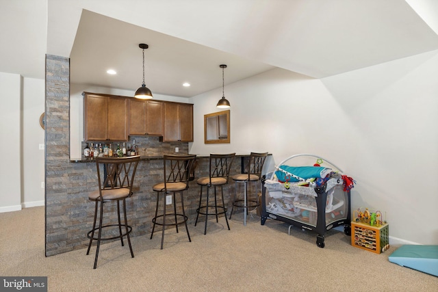 kitchen featuring backsplash, light carpet, a breakfast bar, dark countertops, and decorative light fixtures