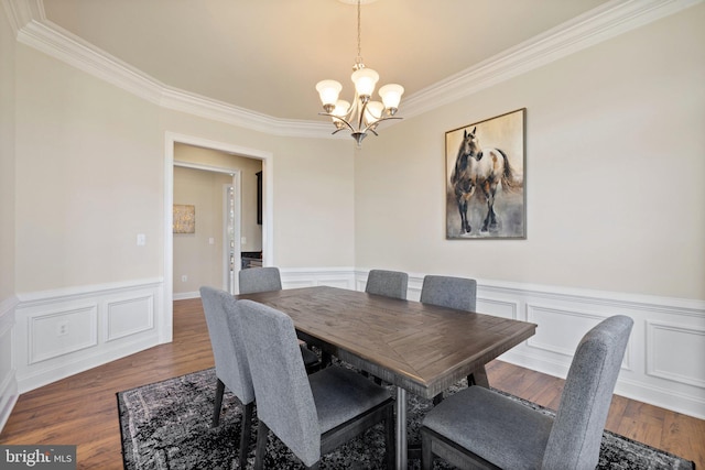 dining space with a wainscoted wall, ornamental molding, wood finished floors, and a notable chandelier